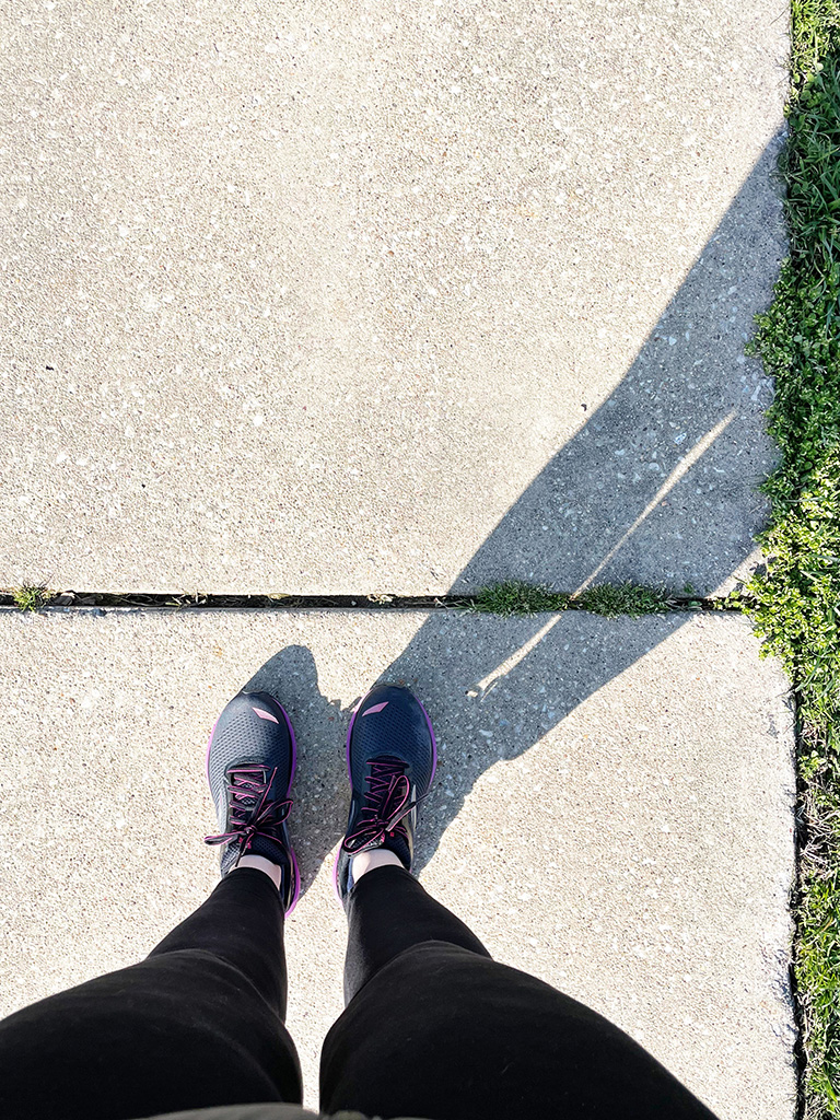 Author's feet in trainers on sidewalk with long shadow