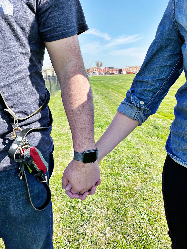 Author holding hands with husband with a background of green grass and blue sky