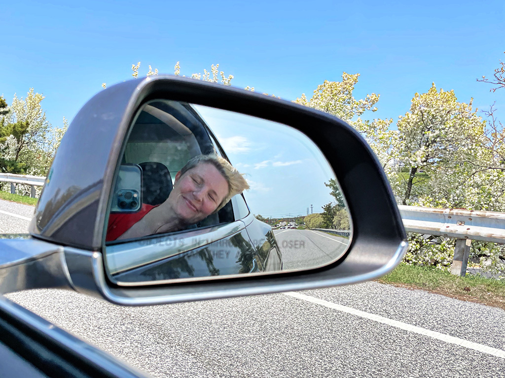 Author's reflection in car's side mirror of head out window