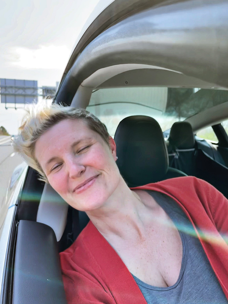 Author with head out car window smiling with eyes closed and hair blowing in wind